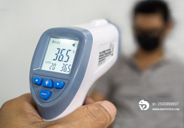 Hand holding infrared thermometer to measuring temperature on blurred asia people with face mask on background. Covid flu screening 19 concept.