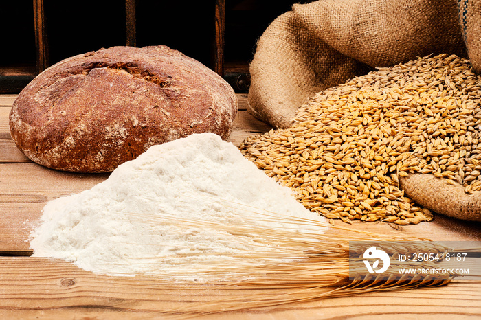 Brot mit Mehl, Getreide und Ähren auf Holztisch