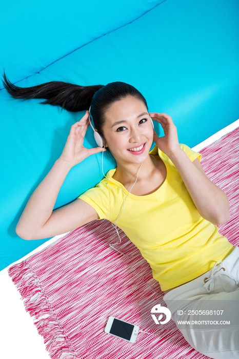 棚拍年轻女人躺在地毯上听音乐