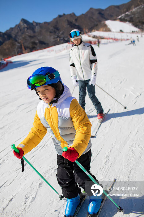 小男孩跟着教练在户外学滑雪