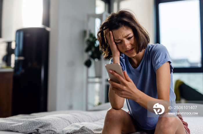 Young woman feeling disappointed while reading text message she received on mobile phone.