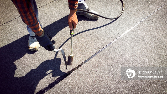 Roofer installing a roll of roofing felt by gas blowpipe torch