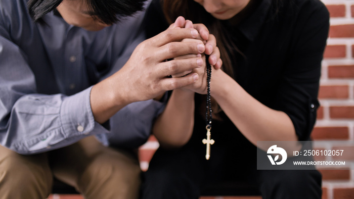 A young Asian Christian couple praying to Jesus Christ in a church.