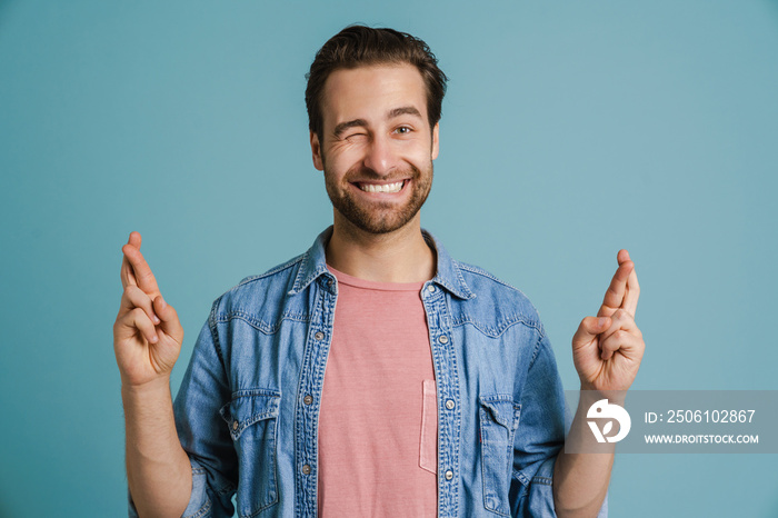 Young bristle man winking and holding fingers crossed for good luck