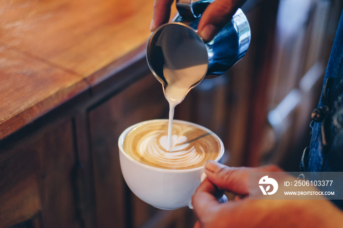 Hand barista pouring milk on coffee latte flower shape in cup