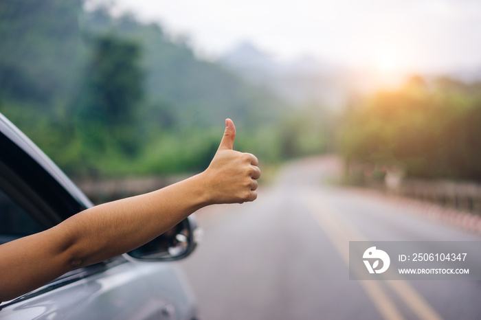 Hand of woman traveler with thumbs up from car form the asphalt road go to travel.