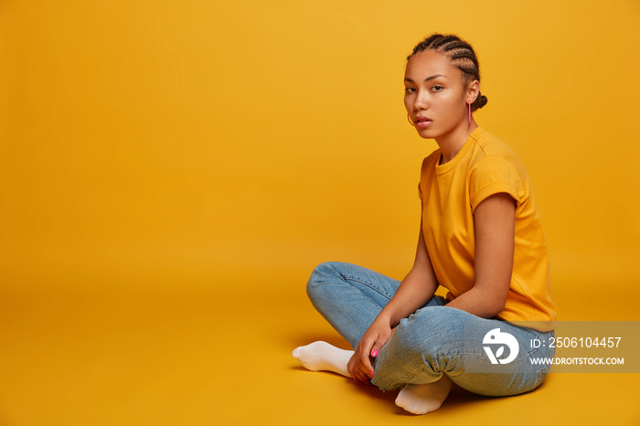 Photo of attractive young female model with cornrow braid hairstyle sits in lotus pose, feels relaxe