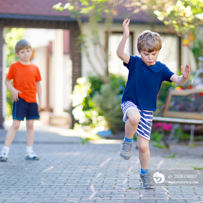 Two little school and preschool kids boys playing hopscotch on playground