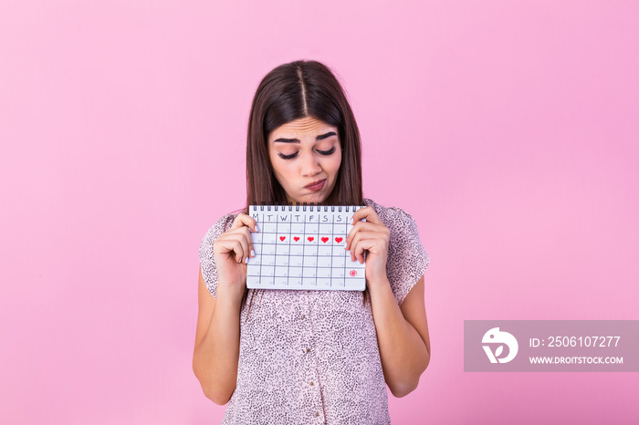 Portrait of disappointed outraged woman 20s holding period calendar isolated over pink background in