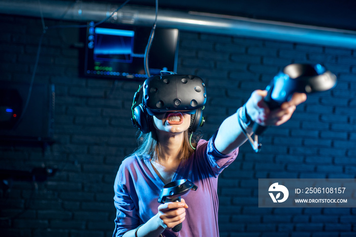 Young woman playing game using virtual reality headset and gamepads in the dark room of the playing 