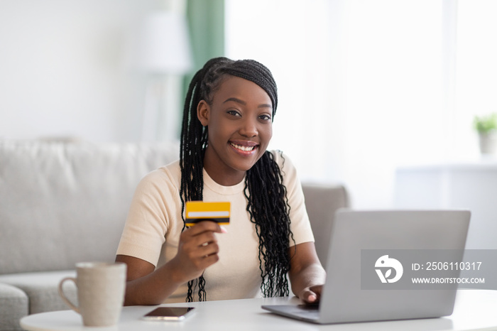 Smiling african woman holding credit card, using laptop