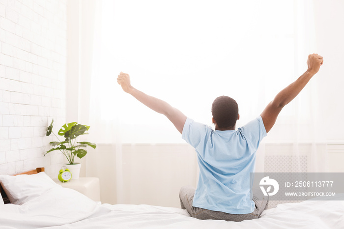 Young man waking up in bed and stretching his arms