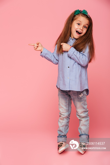 有趣的小女孩用食指指着粉色背景的全长照片