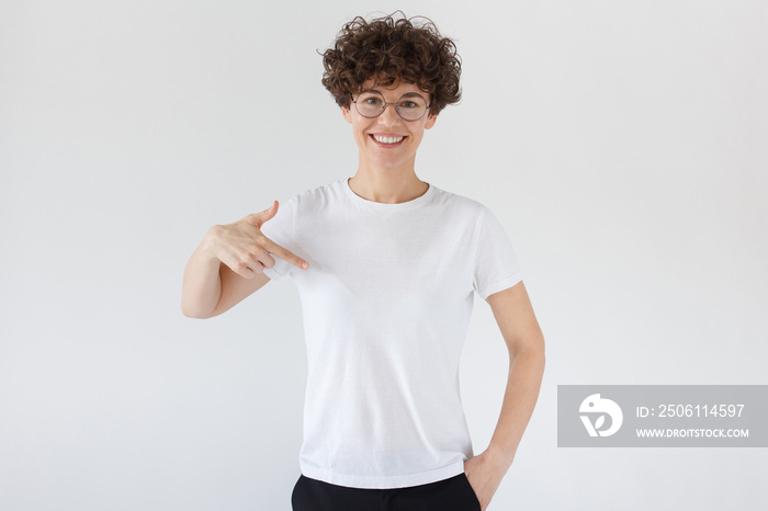 Smiling nice woman pointing at her blank white t-shirt with index finger, copy space for your advert