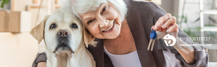 panoramic shot of smiling senior woman embracing dog and holding keys, moving concept