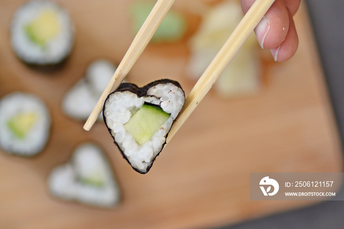 Eat heart shaped sushi with cucumber with chopsticks - close up as a symbol of being in love with su