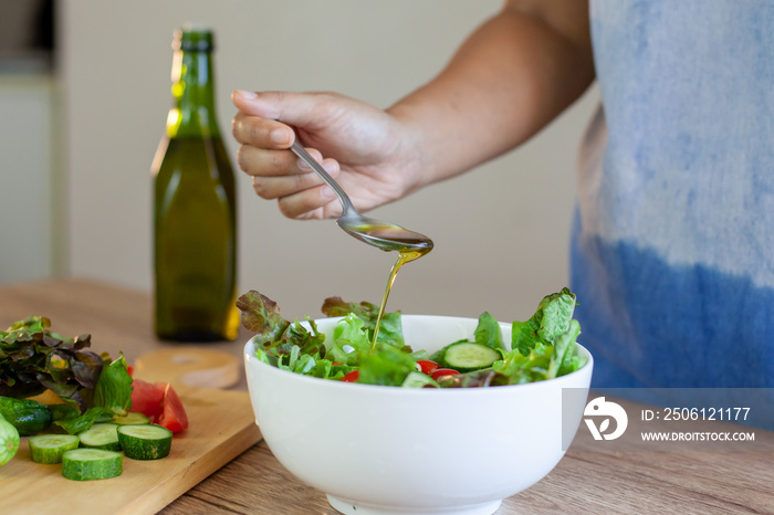 Asian woman pouring olive oil into  fresh vegetable salad bowl in the kitchen