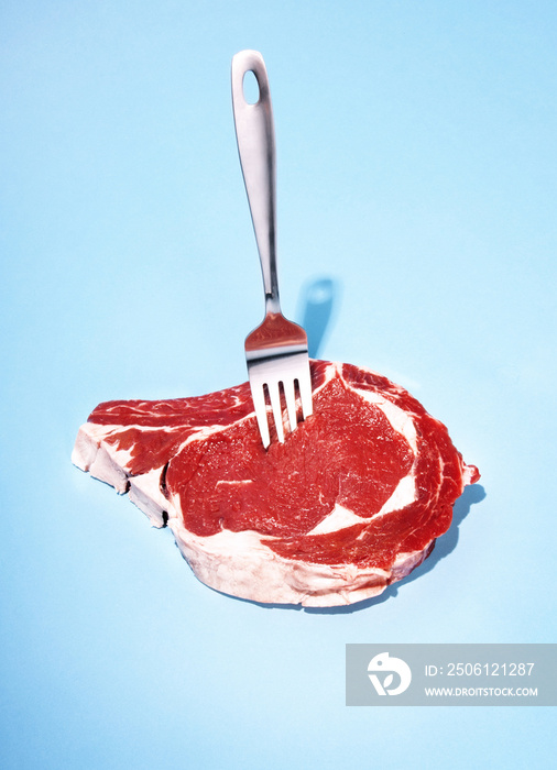 Fork in raw meat against blue background