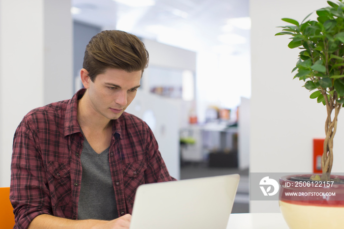 Focused young creative businessman working at laptop in office