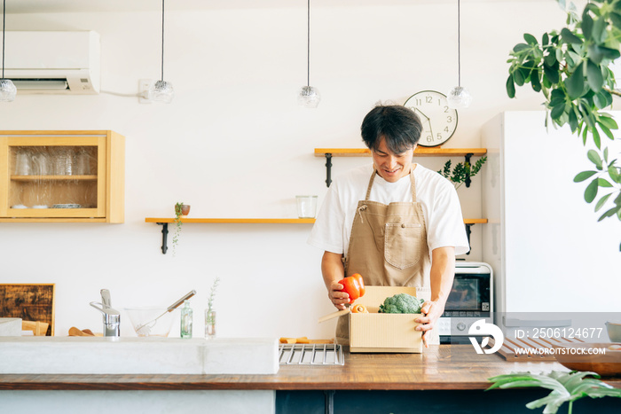 キッチンでダンボールに入った野菜を持つ男性