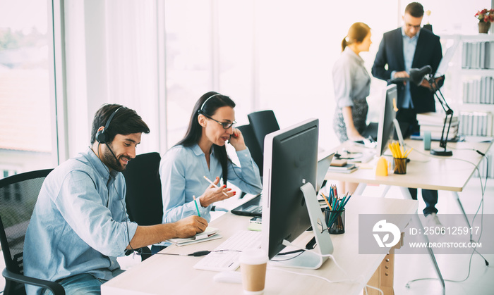 Attractive business people in headsets are smiling while working with computer in modern office