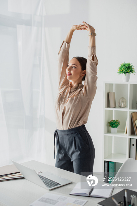 beautiful young businesswoman stretching arms in modern office with laptop