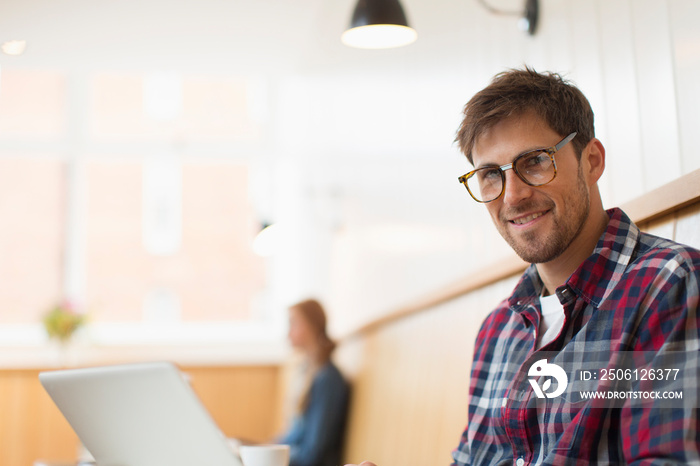 Portrait confident man working at laptop in cafe