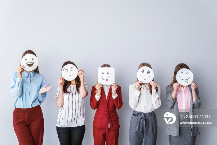 Group of woman covering their faces with drawn emoticons against light background