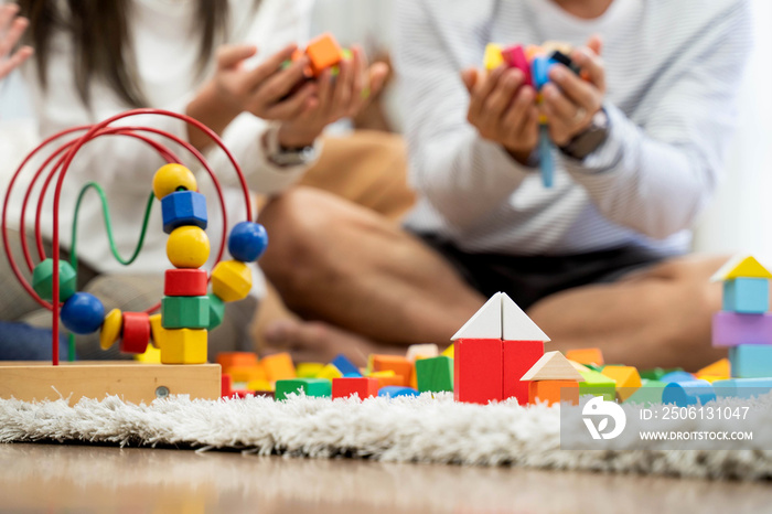 Happy young father and mother and a little daughter playing with Toy wooden blocks, sitting on the f