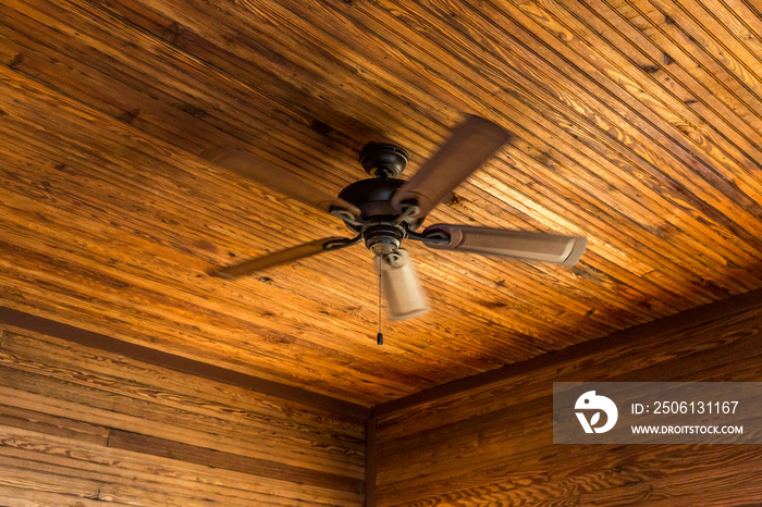 Rustic wood-paneled cabin or lodge walls and ceiling with a fan