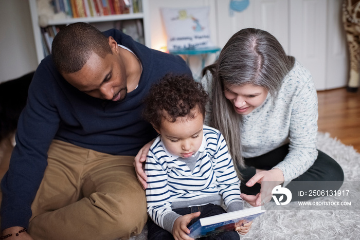 Cute son holding book while sitting with parents on rug at home