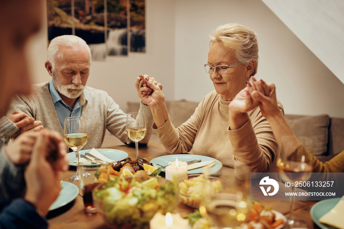 一位老年妇女和她的家人在餐桌前闭着眼睛祈祷。