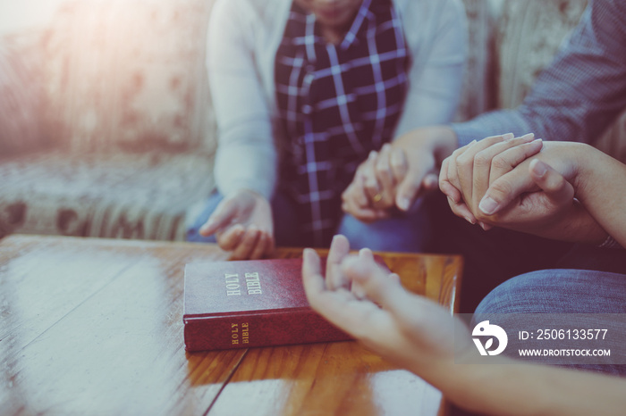 Close up of  people group holding a hand and pray together over a blurred holy bible on wooden table