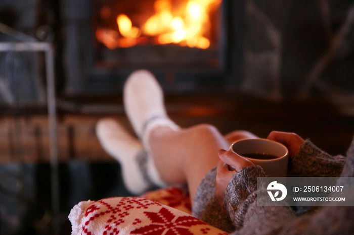 Woman resting with cup of hot drink near fireplace