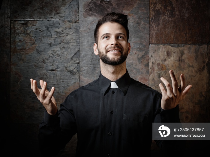 Portrait of handsome young catholic priest preaching looking up smiling.