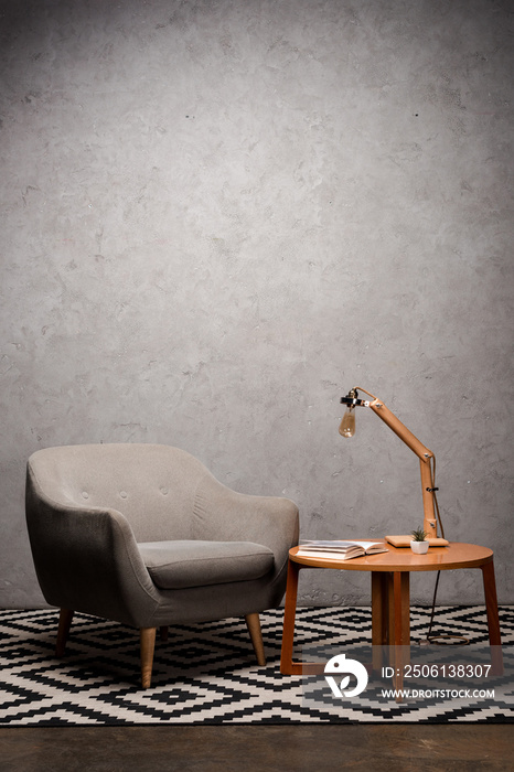 interior of living room with comfortable grey modern armchair near wooden table and lamp on carpet