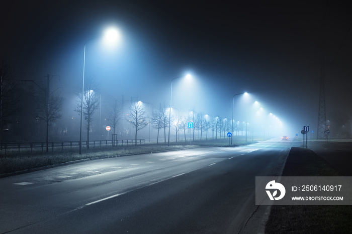 Illuminated empty highway in a fog at night. Street lights and road signs close-up. Dark urban scene