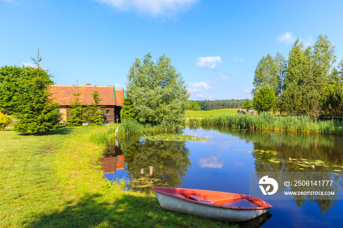 Fishong boat on shore of small pond and old traditional rural house in Galkowo village near Krutynia