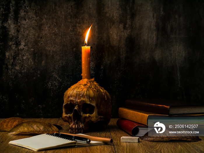 A wizard working desk with candle on the human skull, books of magic, note book and stationary.