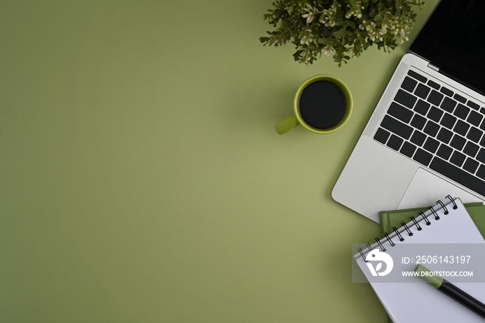 Mockup laptop computer, coffee cup, glasses and notebook on green background. Flat lay, top view.