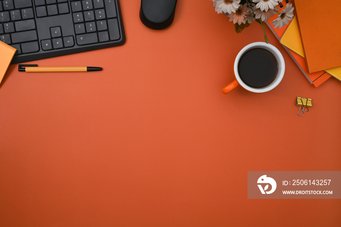 Top view stylish workspace with wireless keyboard, coffee cup and notebooks on orange background.