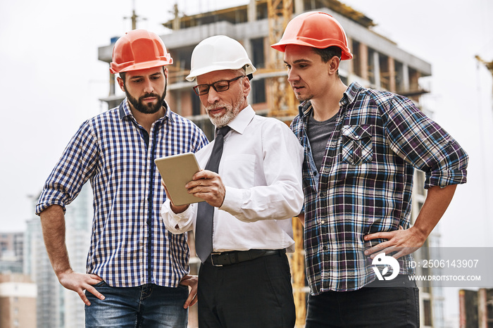 Using modern technologies. Senior engineer is looking at project plan on digital tablet with two you