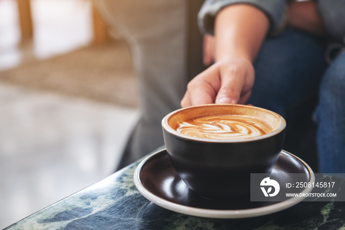 Closeup image of a hand holding a cup of hot coffee on table