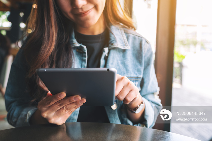 Closeup image of a woman holding and using tablet pc while sitting in cafe