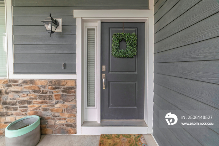 Entrance to a house with side light and gray front door decorated with wreath