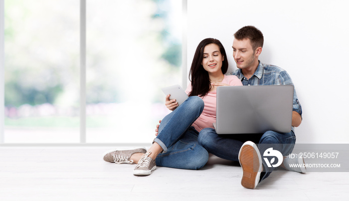 快乐的年轻夫妇坐在地板上，拿着笔记本电脑寻找他们的新家和家具。模仿