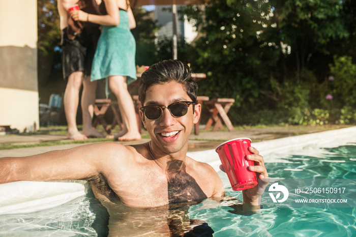 Young man with red cup in swimming pool