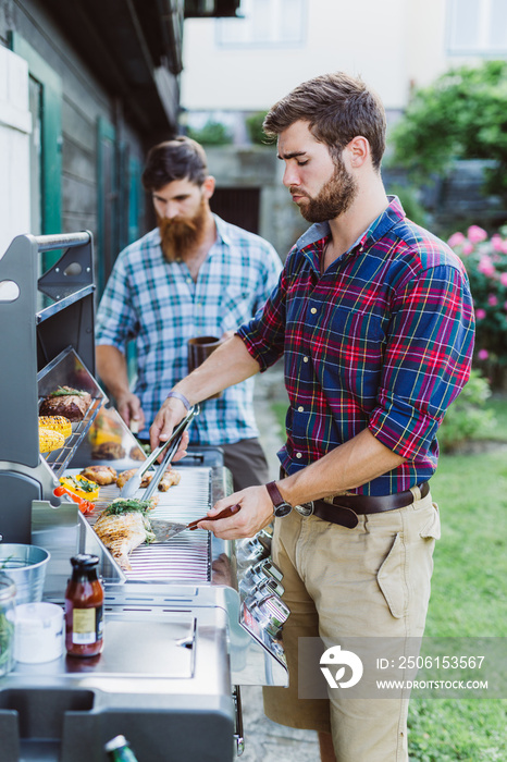 Two men cooking outdoors at barbecue station having fun