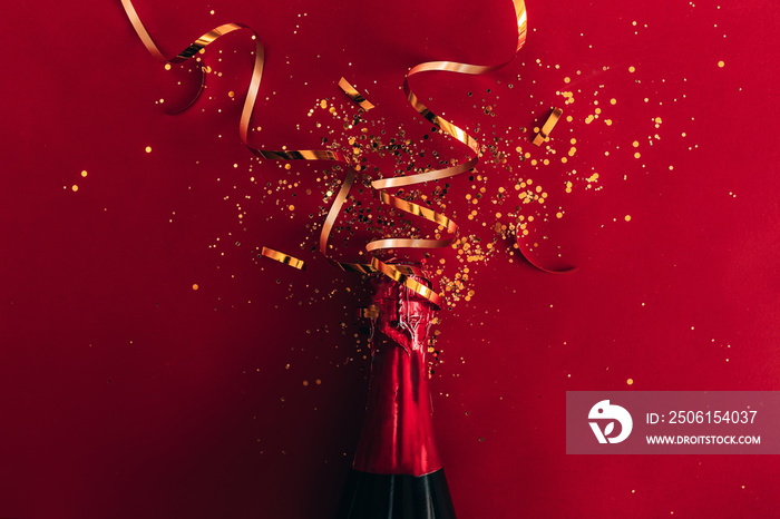 Bottle of red champagne with gold glitter, sparkles, confetti on red background, top view. New year 