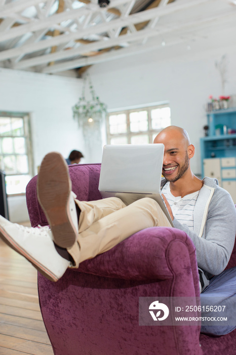 Happy young man using laptop in armchair